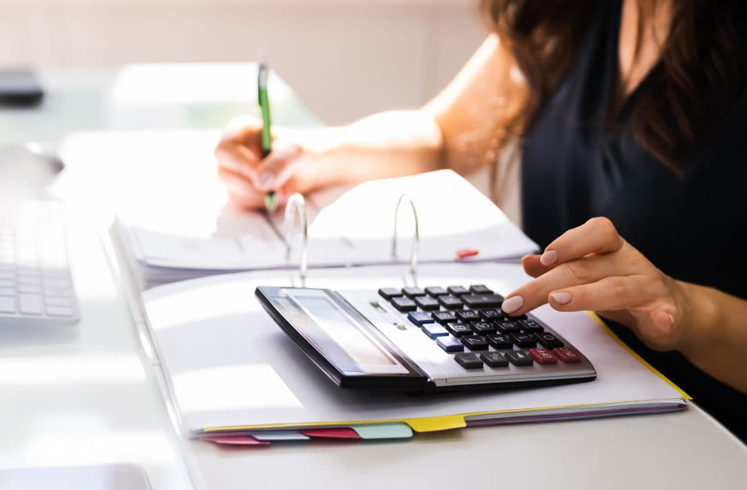 Personne utilisant une calculatrice et prenant des notes sur un bureau, illustrant des activités liées à la comptabilité ou à la gestion financière.